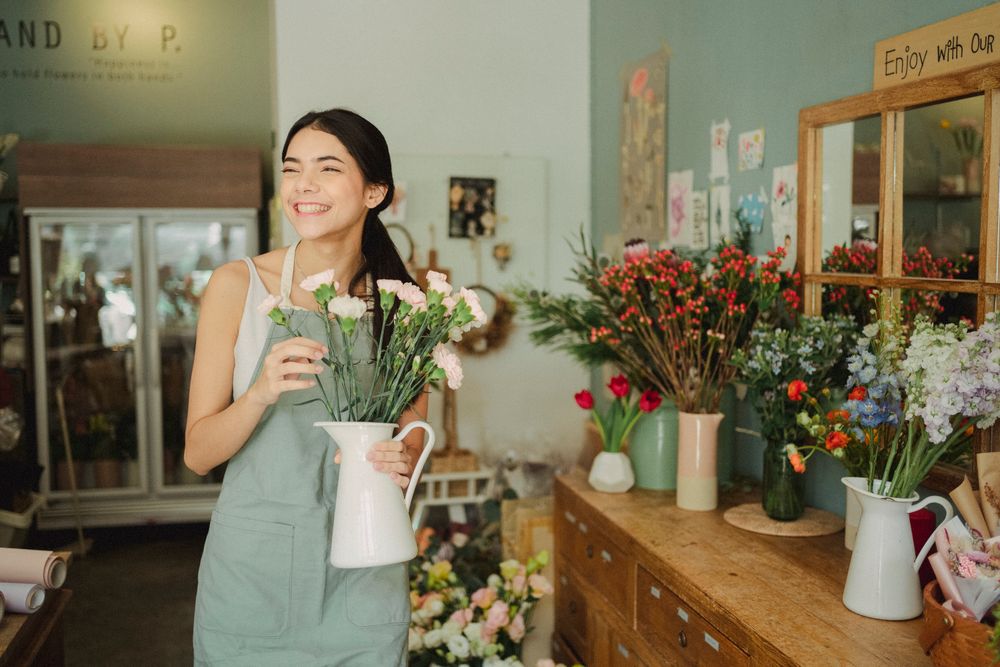 A young shop owner laughing while arranging flowers in her pastel green studio